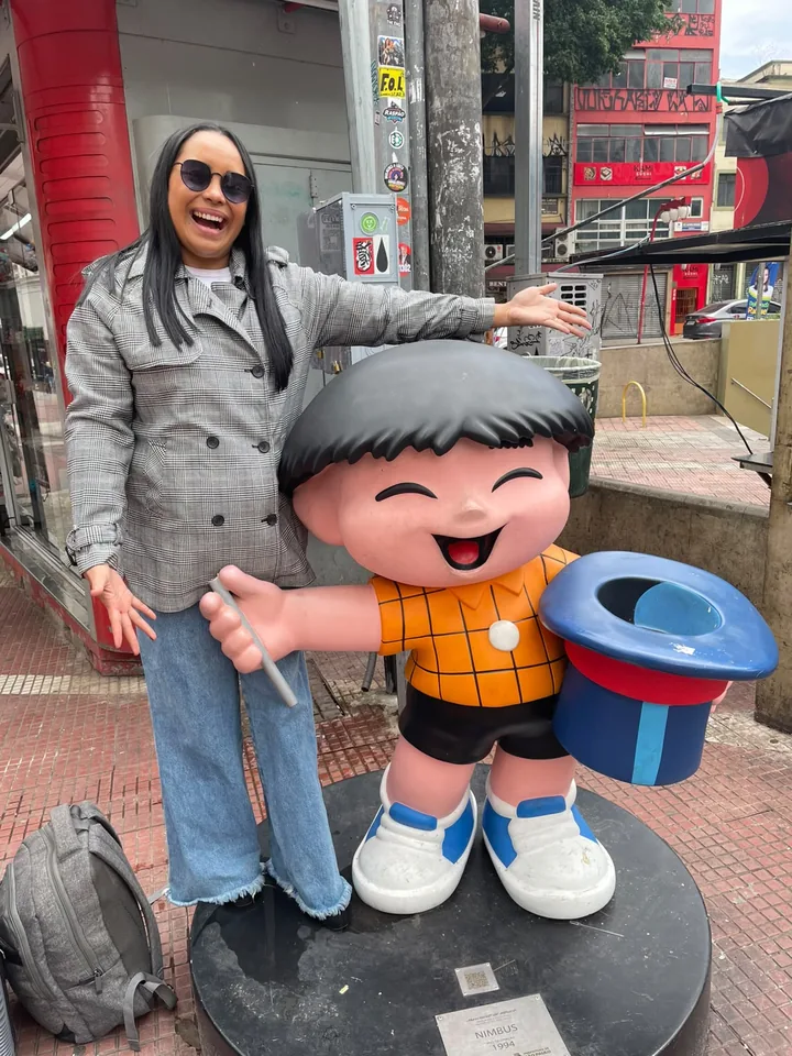 Cliente Quero+ Viagens sorrindo ao lado de escultura colorida em rua de São Paulo